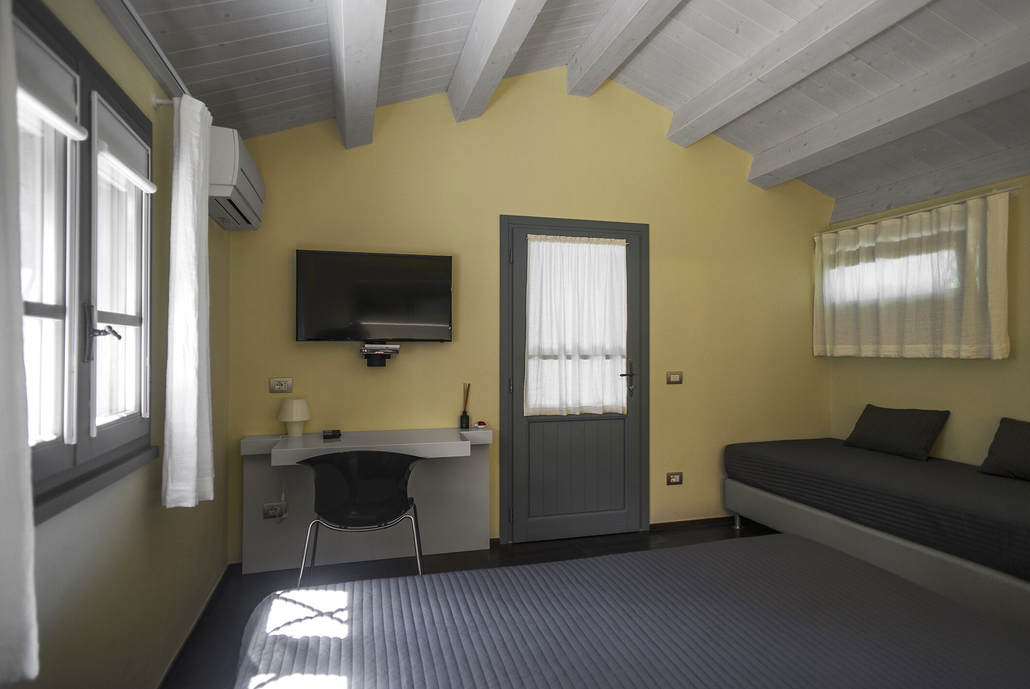 A bedroom with a bed, a desk, a chair, a television, and a door.