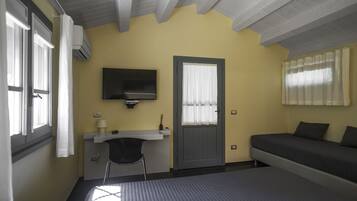 A bedroom with a bed, a desk, a chair, a television, and a door.