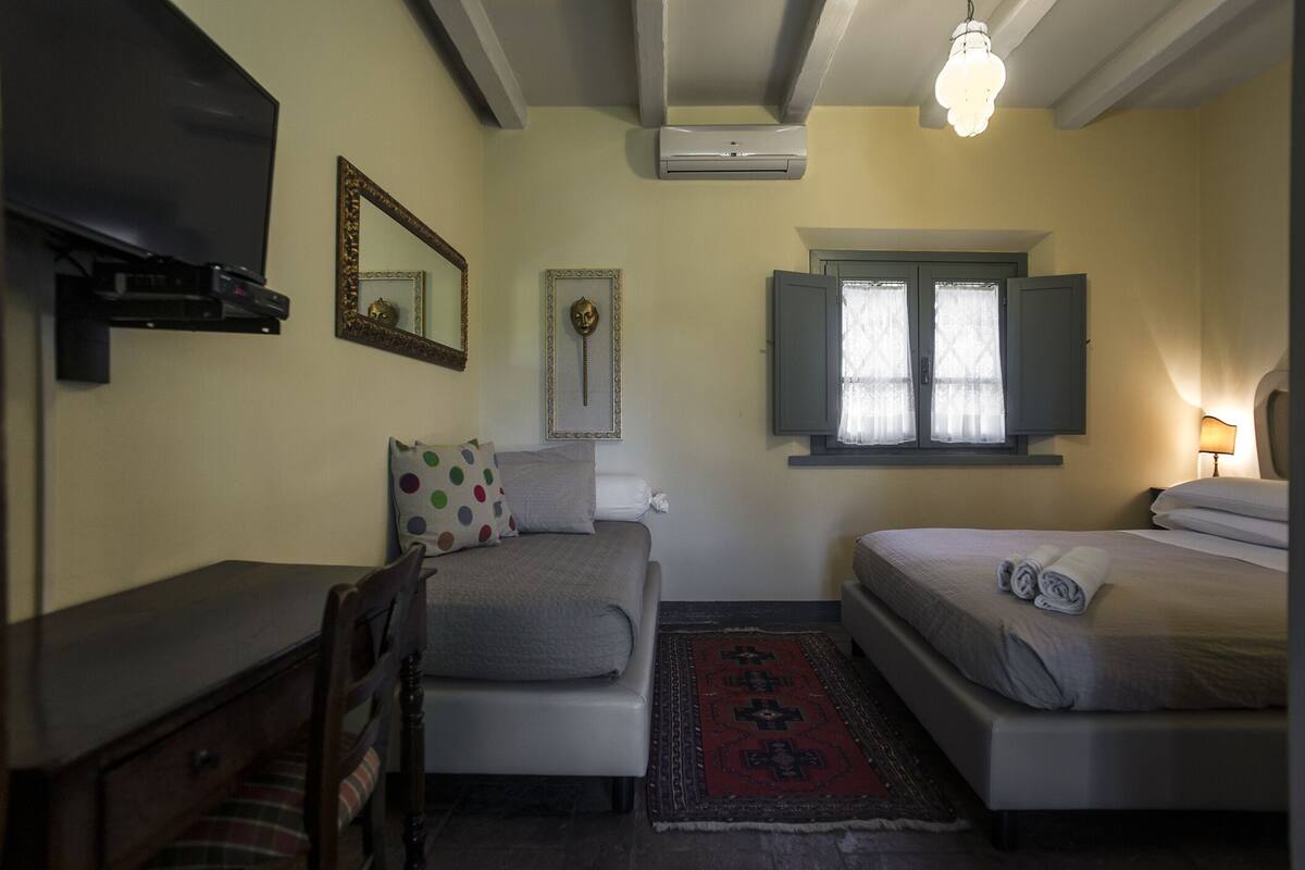 Une chambre avec deux lits, un bureau, une chaise, une t élévision, un miroir et une fenêtre avec des rideaux.