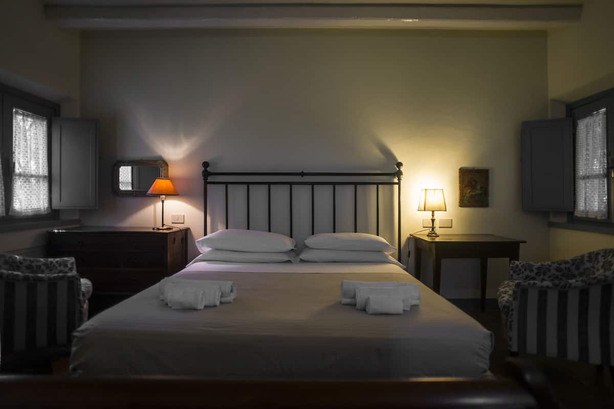 Un lit bien fait, avec des oreillers et des serviettes, deux lampes de chevet, un miroir et une petite table avec une lampe.