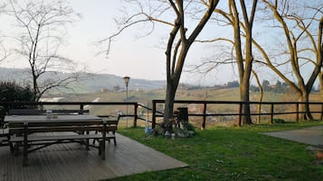 Una terrassa de fusta amb taula de picnic i bancs, envoltada per una tanca de fusta i arbres.