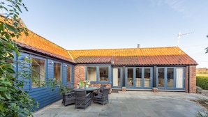 Una casa con fachada azul, techo de tejas y un patio con mobiliario exterior.