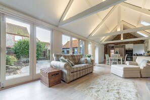 A spacious living area with a large sofa, a smaller sofa, and a fluffy rug. There is a wicker basket and a dining table with chairs.