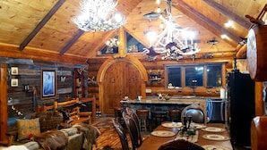 L’intérieur d’un chalet rustique, avec un coin repas en bois, des murs en pierre et une grande porte en bois.