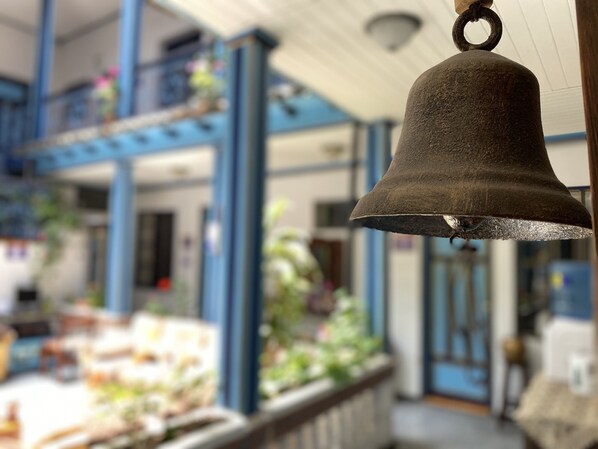 A bell hanging in a room with blue columns and a window overlooking a garden.