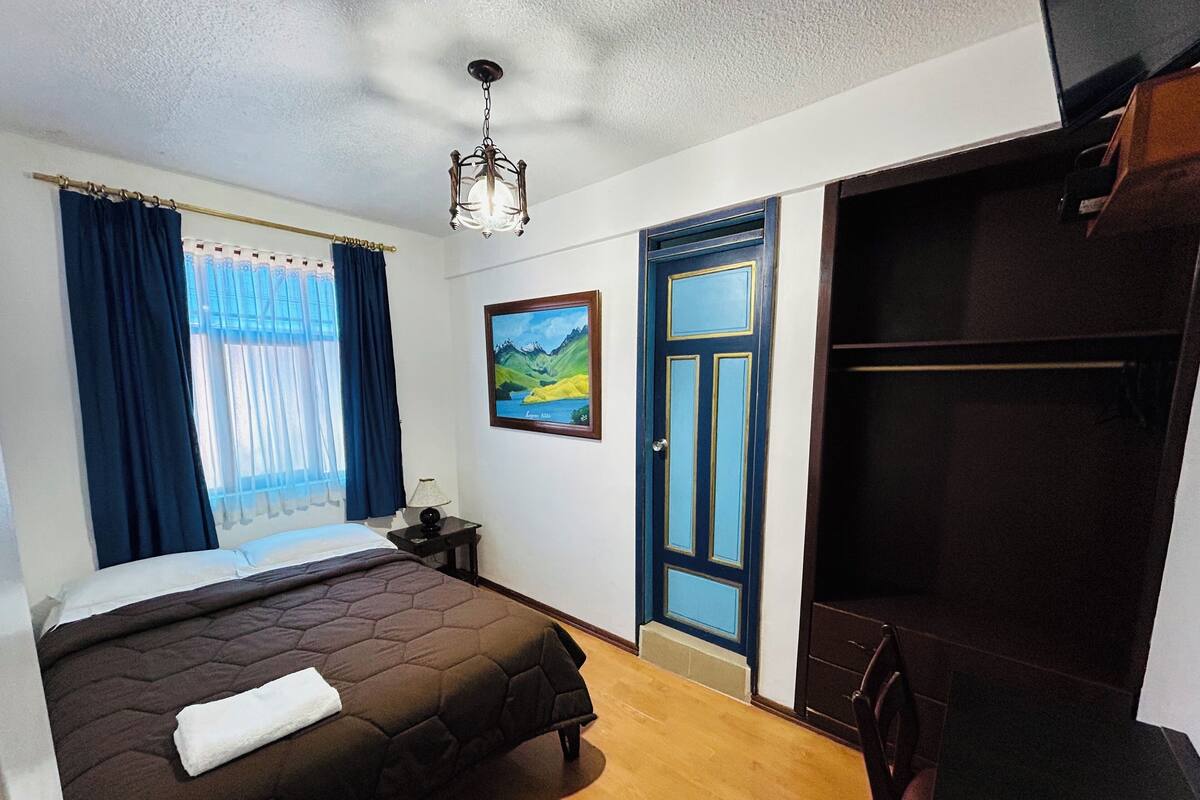 A bedroom with a bed, a nightstand, a painting, a wardrobe, and a door.