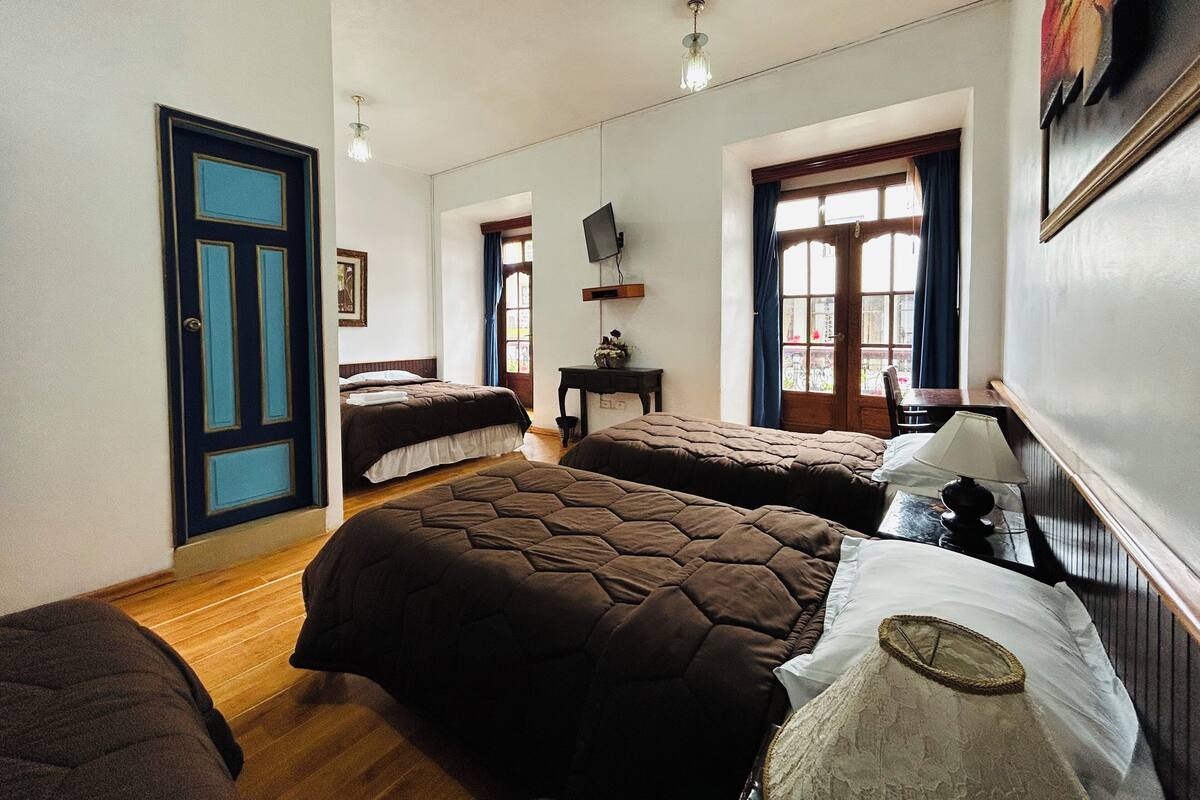 A bedroom with two beds, a desk, a TV, and a window with curtains.