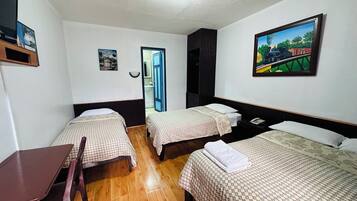 Habitación de hotel con dos camas individuales, piso de madera, escritorio y una silla. Hay un cuadro en la pared y una puerta que da a un baño.