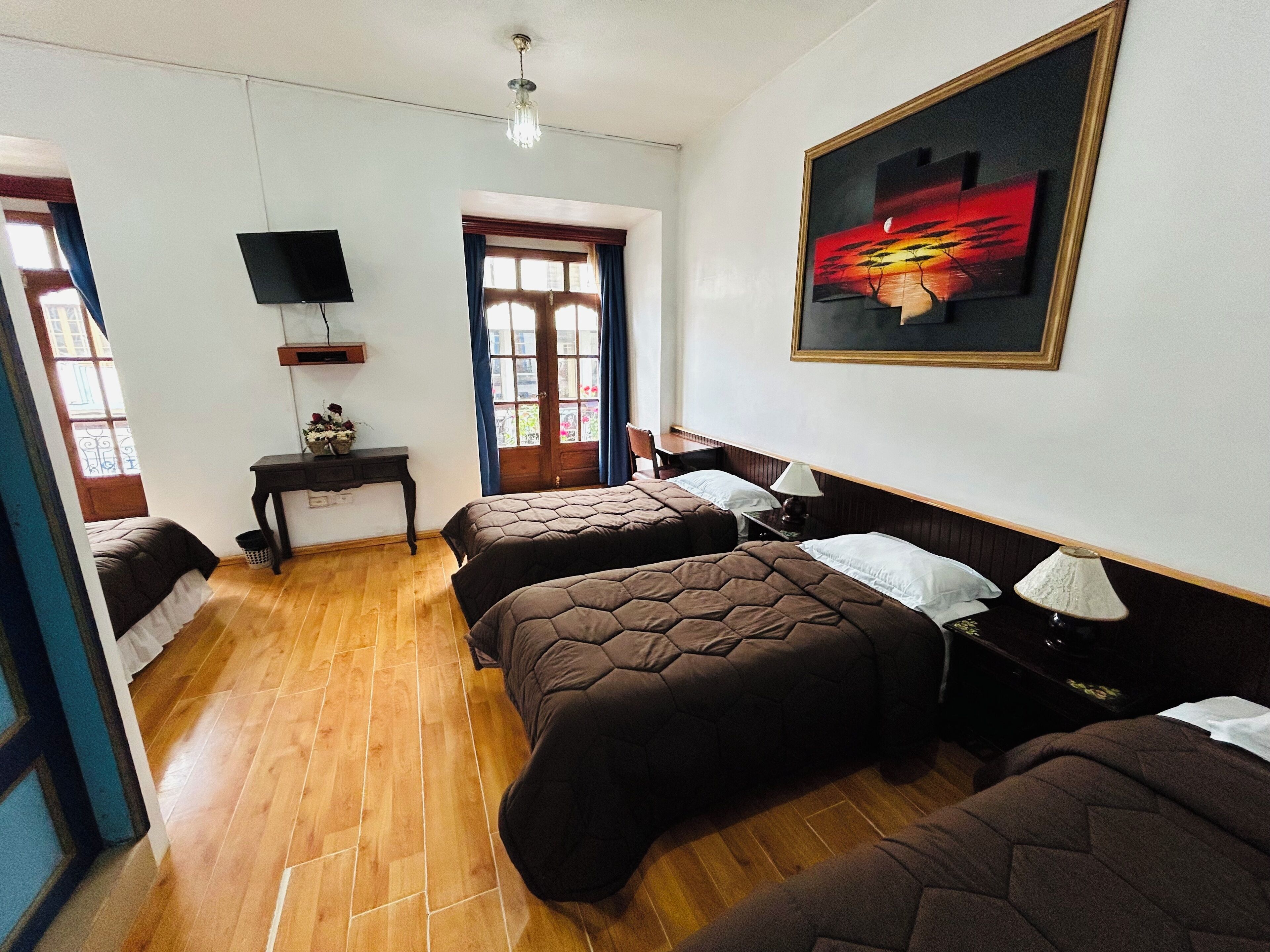 Habitación de hotel con dos camas, un escritorio, un televisor, una ventana con cortinas y un cuadro en la pared.