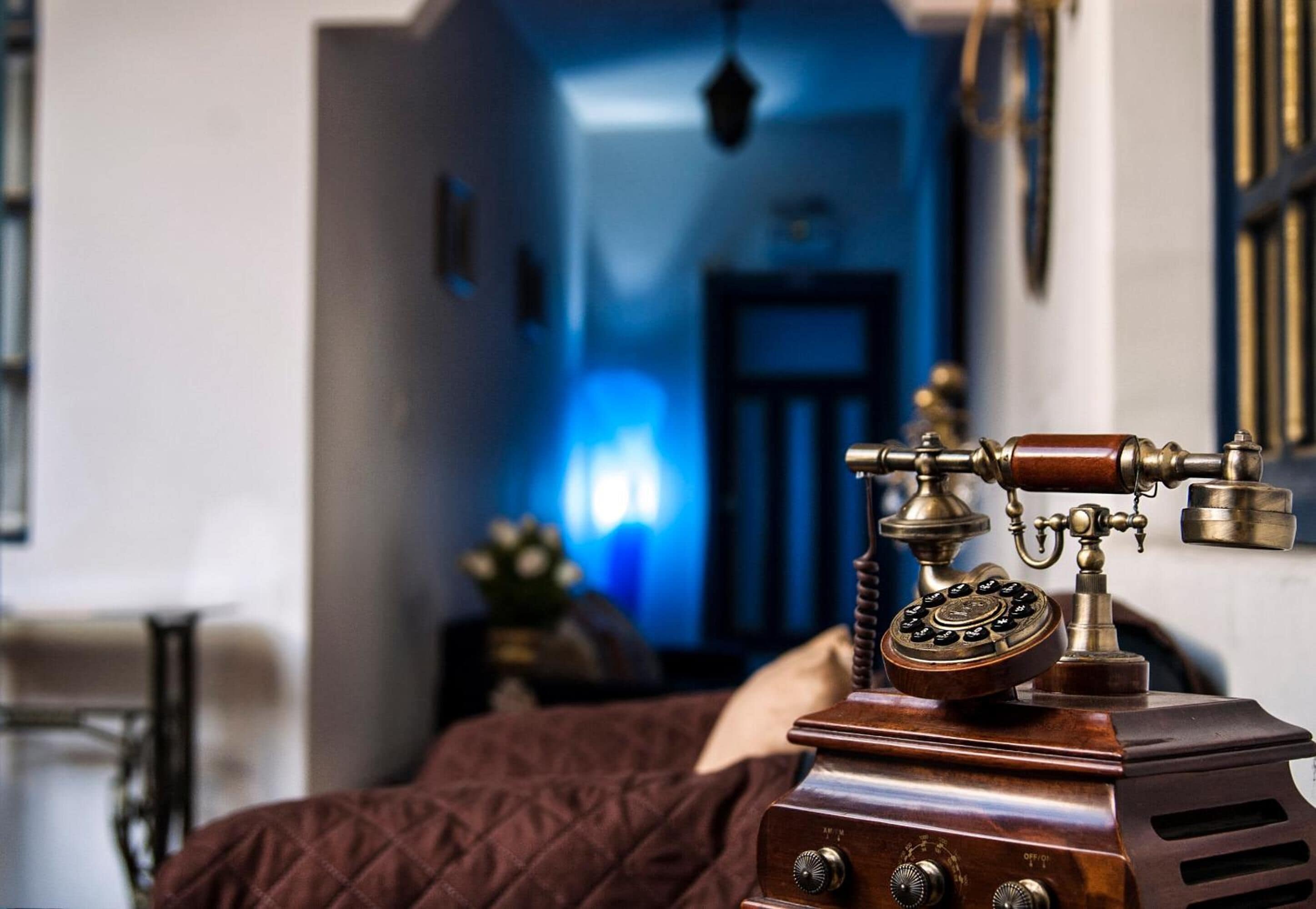 A vintage telephone on a bedside table in a room with a blue-lit hallway.