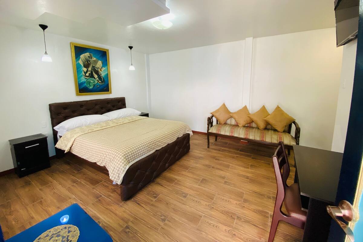 A bedroom with a bed, a sofa, a desk, and a painting on the wall.