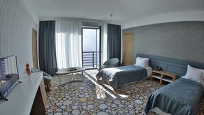 A hotel room with two beds, a desk, a chair, and a view of the sea. - Yurd Hotel (?lisu)