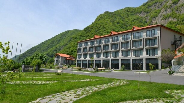 A modern hotel with multiple floors, large windows, and a red roof, situated in a mountainous area with lush greenery. - Yurd Hotel (?lisu)