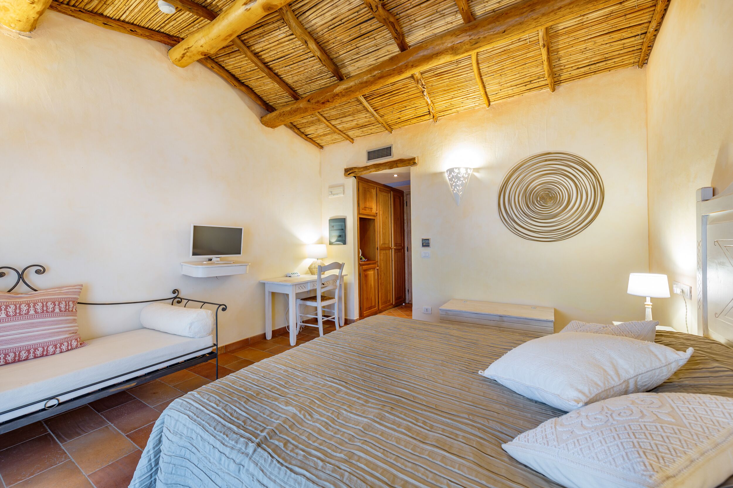 Un dormitorio con cama, escritorio, silla, televisor y lámpara fijada a la pared.