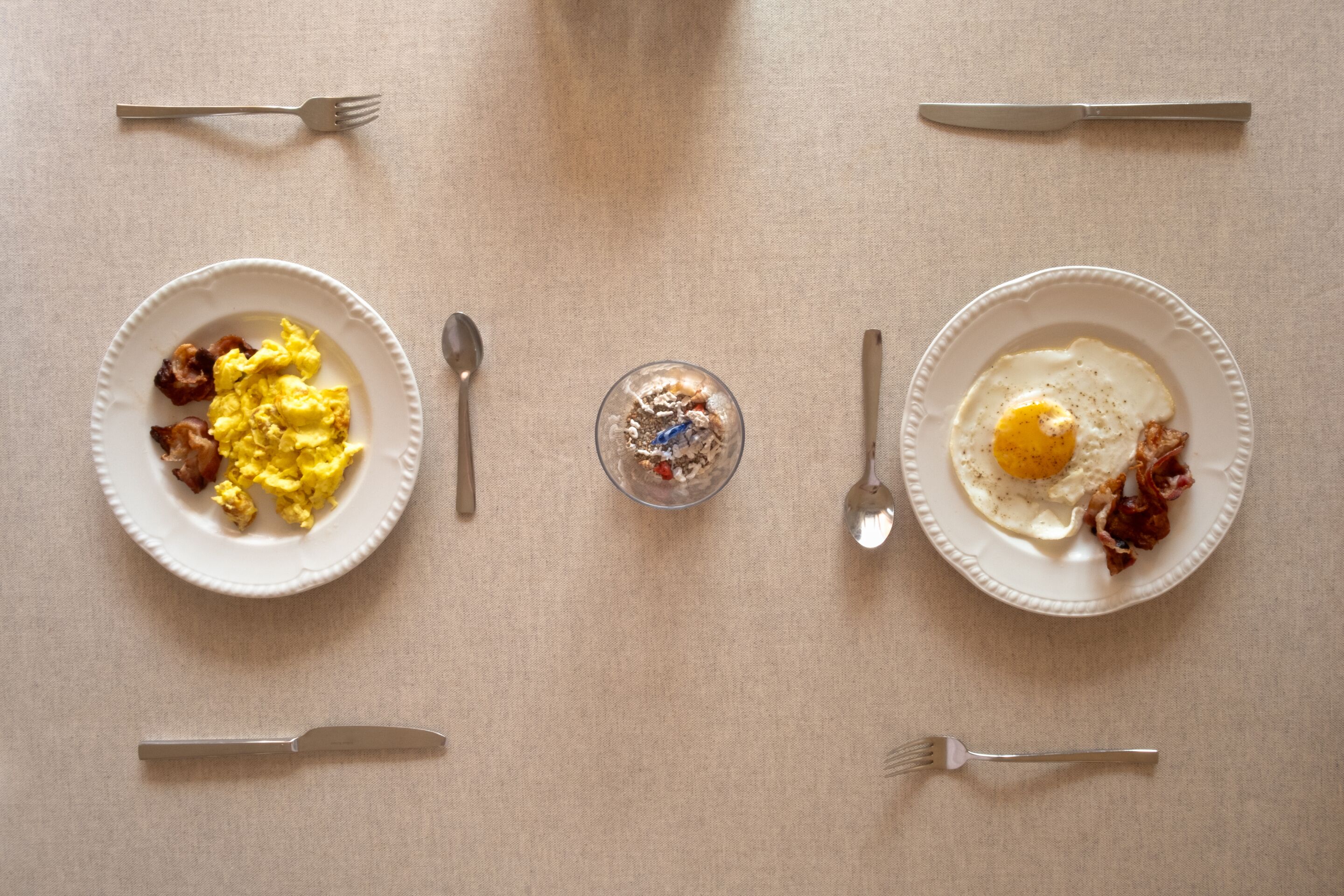 Deux assiettes de nourriture pour le petit-déjeuner sont posées sur une table, avec des couverts à proximité.