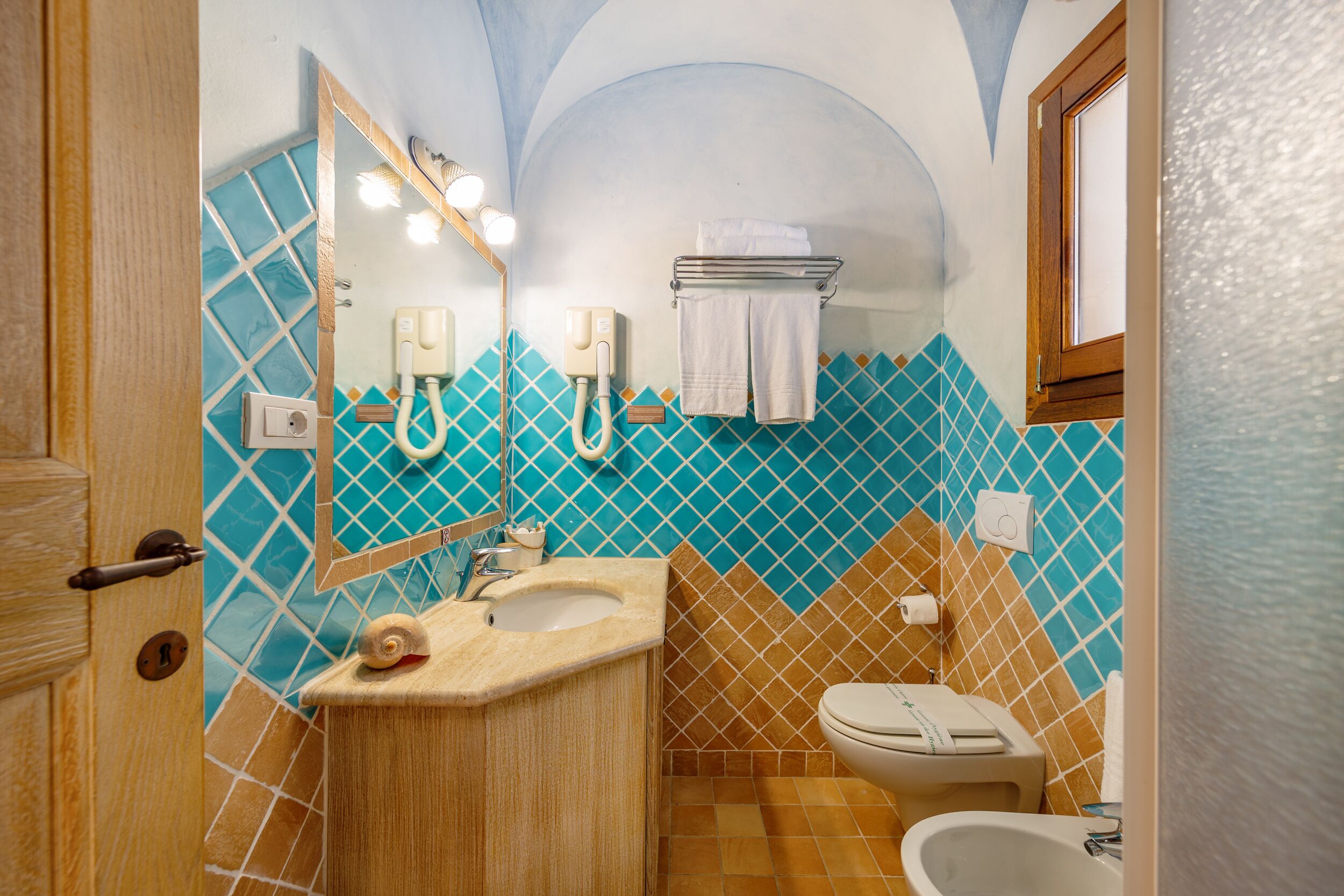 Een badkamer met een wastafel, spiegel, handdoekhouder, toilet en een bidet.
