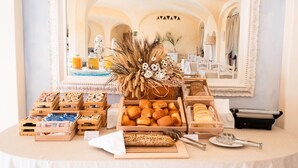 A buffet table with various breads and pastries, a decorative centerpiece, and a mirror reflecting the room's architecture. - Moma Hotel Cannigione (Arzachena)