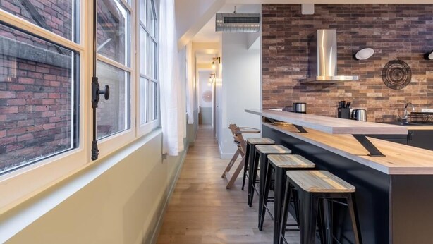 Une cuisine moderne avec un mur de briques en guise de crédence, un plan de travail en bois et des tabourets de bar.