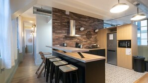 Une cuisine moderne dotée d’un îlot central, de tabourets de bar, d’une hotte en acier inoxydable et d’un réfrigérateur.