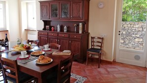 A dining area with a wooden table set for a meal, a cabinet with glass doors, and a stone wall outside. - Case Vacanze Borgo Faraldi - La Bottega del Fabbro (Villa Faraldi, Liguria)