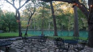 An outdoor patio with stone flooring and metal furniture, overlooking a lake.
