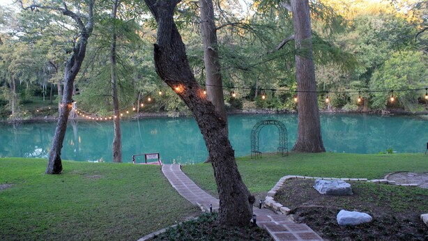 A serene lakeside setting with a paved walkway, trees, and string lights.