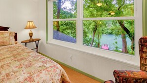 A bedroom with a large window, a bed, a chair, and a lamp.