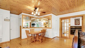 A dining area with a wooden table and chairs, a ceiling fan, and a view into the kitchen through a large mirror.