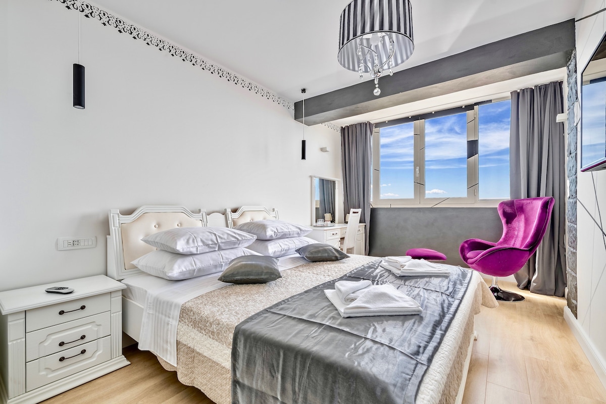 Un dormitorio moderno con una cama grande, mesitas de noche, tocador y ventana con cortinas.