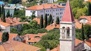 Une ville côtière aux toits recouverts de tuiles rouges, dotée d’un imposant clocher et de bâtiments entourés de verdure.