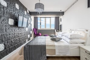 A modern bedroom with a stone wall, a bed with white bedding, a purple chair, and a large window with a view. - Charming Spalato Rooms (Split)