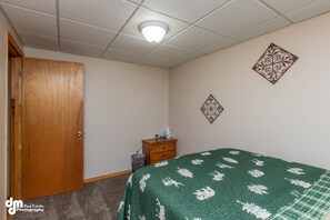 Une chambre avec une porte en bois, une petite commode en bois, une couvre-lit verte et des œuvres d’art décoratives accrochées au mur.
