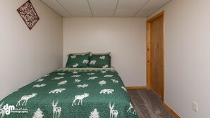Un dormitorio con una colcha de cama de motivos animales en tonos verdes, una puerta de madera y una alfombra pequeña.