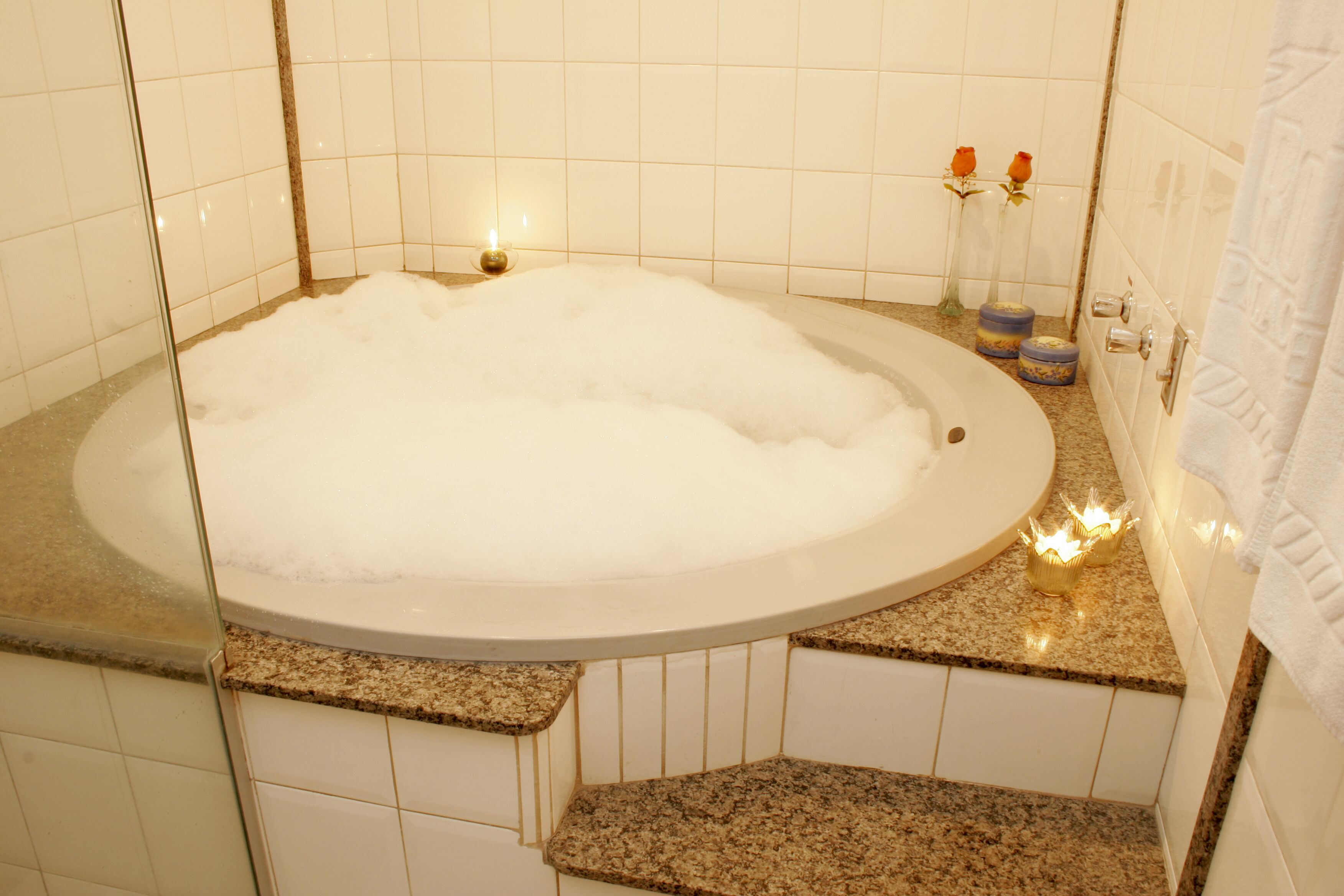 Een badkamer met een groot bad vol bubbels, een wastafel met spiegel en een handdoekhouder.