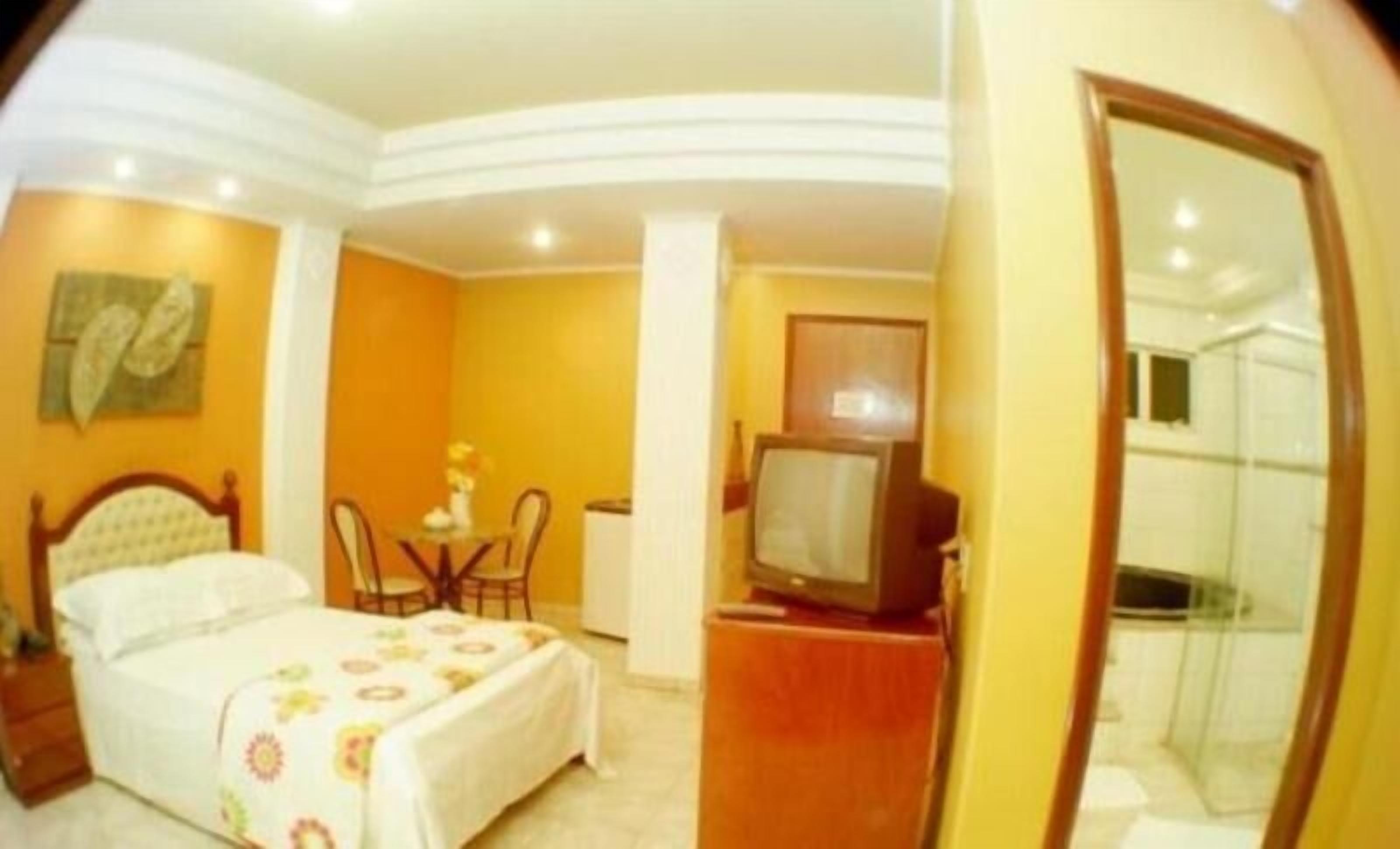 Habitación de hotel con cama, escritorio, silla, televisión y baño visible a través de una puerta de cristal.