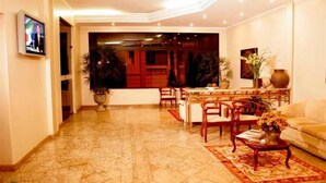 Amplia sala de estar con piso de mármol, una mesa de comedor con sillas, un sofá y varias plantas en macetas.