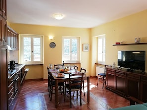 Un coin repas avec une table dressée pour quatre personnes, un téléviseur et un espace cuisine équipé de placards et d’une cuisinière.