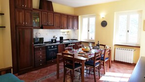 Een keuken met houten kastjes, een eettafel met stoelen, een koffiezetapparaat en een raam met uitzicht.