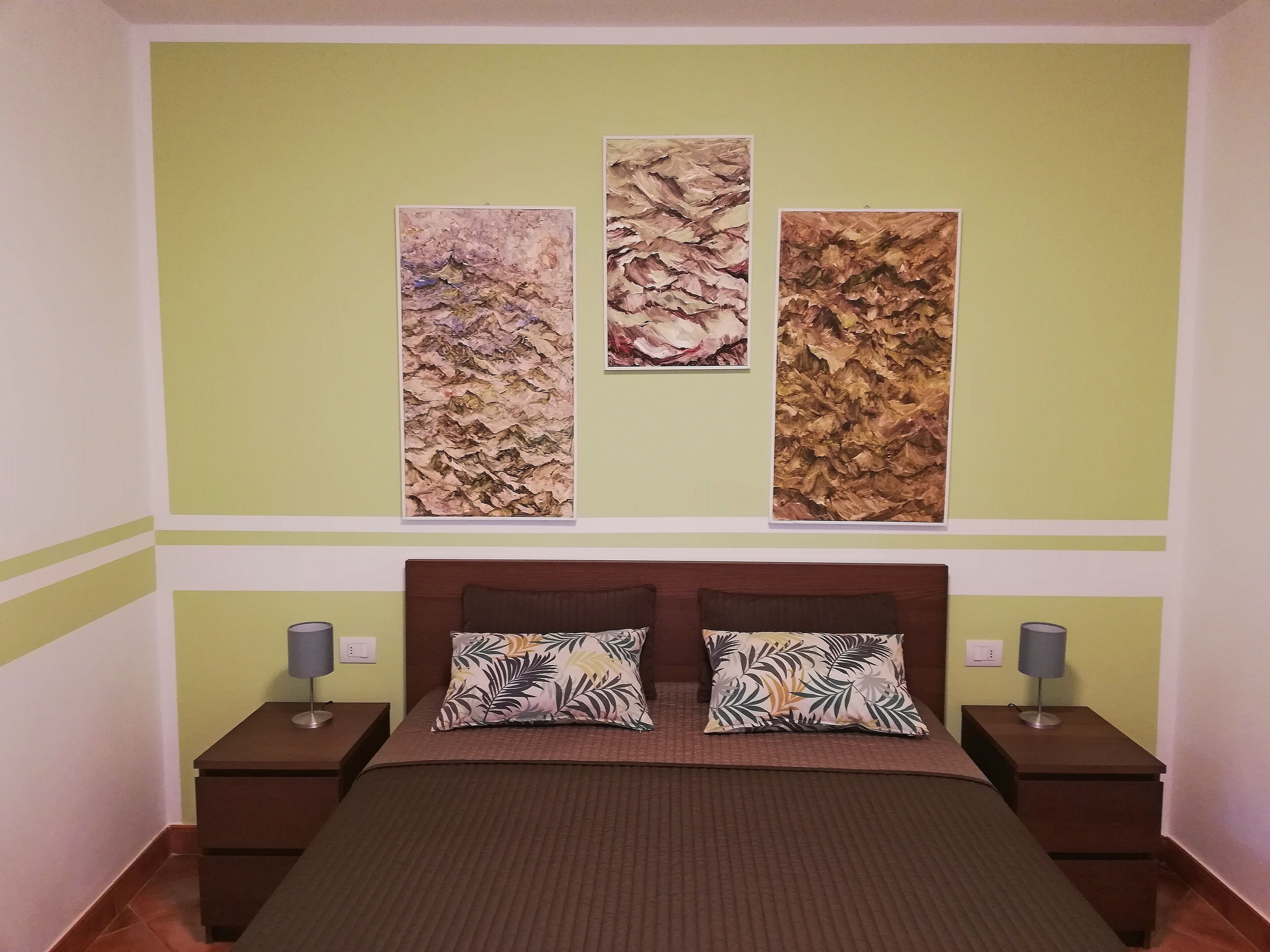 A bedroom with a bed, two nightstands, and three vertical wall art pieces.