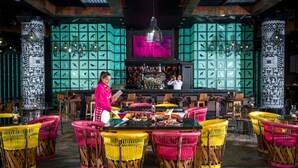 Un restaurant avec des chaises en osier aux couleurs vives, un bar avec un barman et, au fond, des aquariums décoratifs.
