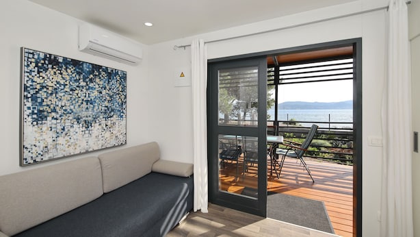 A modern room with a sofa, a large abstract painting, and a sliding glass door leading to an outdoor deck with chairs and a table.