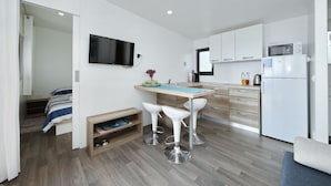 A compact kitchen with a microwave, a sink, and a small refrigerator. There is a bar stool seating area and a television mounted on the wall.