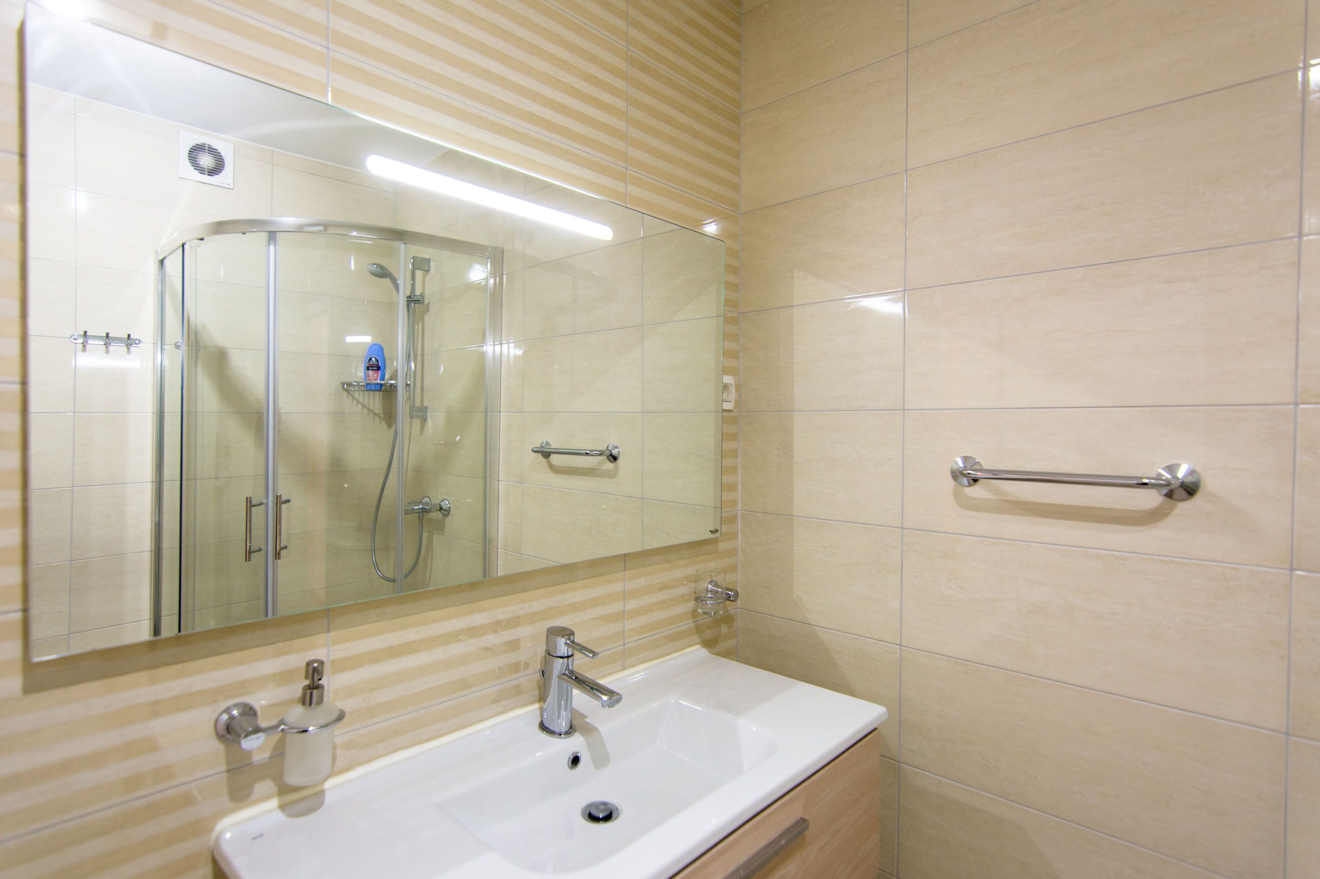 A bathroom with a glass-enclosed shower, a white sink, and a mirror.