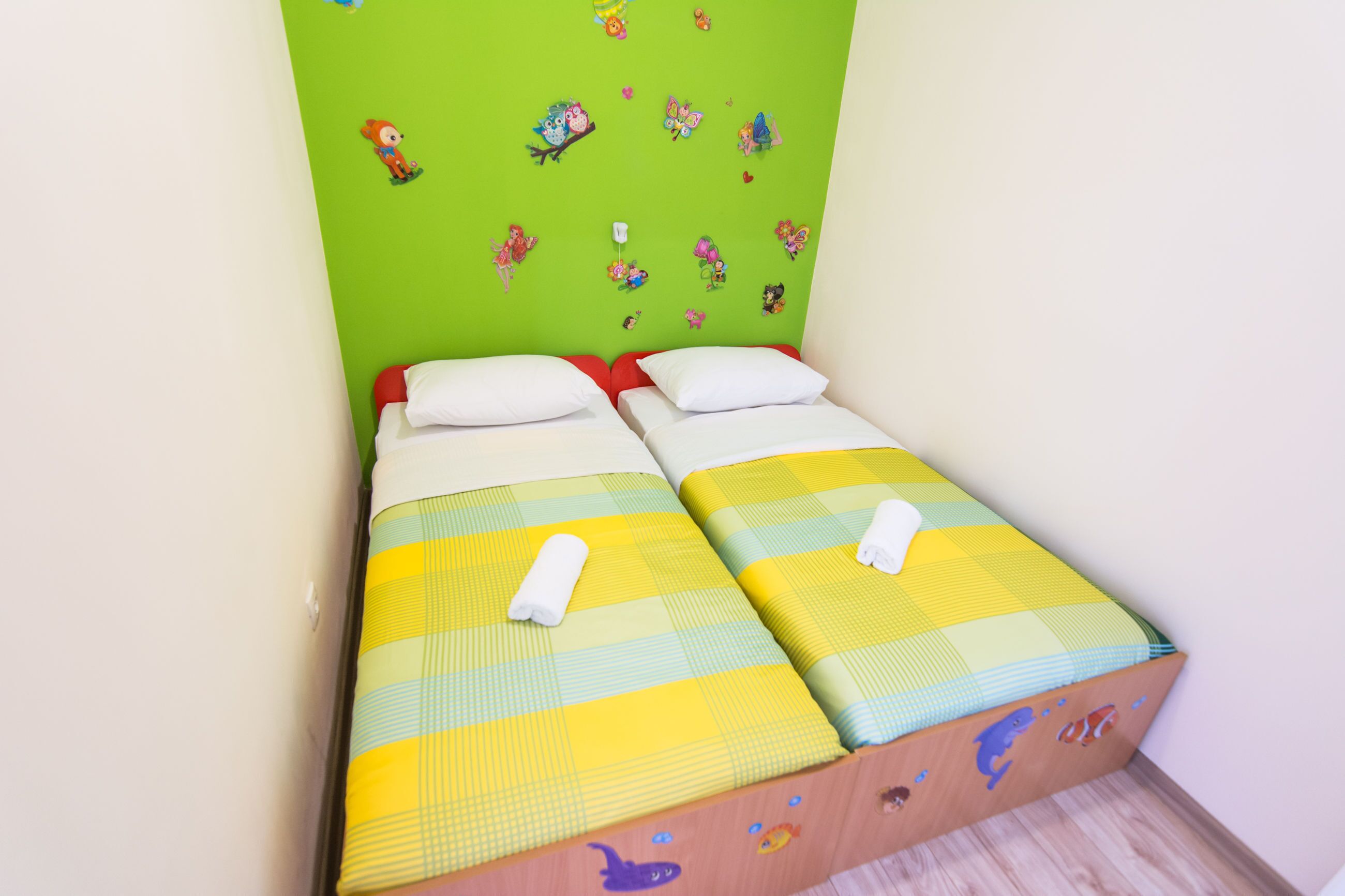 Ein Doppelbett mit einer gelb-grün karierten Tagesdecke, weißen Kissen und einer grünen Wand mit verschiedenen Aufklebern.