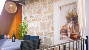 A stone wall interior with a wooden door, a staircase with a potted plant, and a table with wine glasses and a bottle. - Apartments Tarragon (Ugrinic)