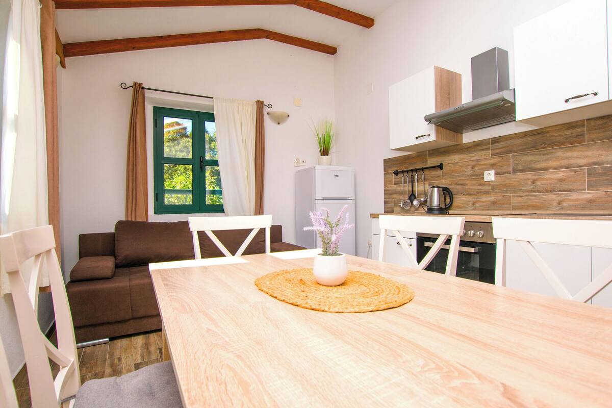A cozy room with a wooden dining table, a white refrigerator, a kitchen area with wooden cabinets, and a brown sofa.