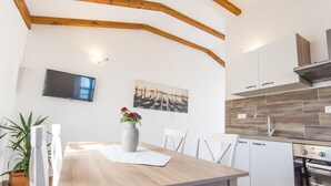 A modern kitchen with wooden beams, white cabinets, a built-in oven, and a large window. - Apartments Tarragon (Ugrinic)