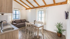 A modern kitchen with wooden beams, a dining area with a table and chairs, a sofa, and a potted plant. - Apartments Tarragon (Ugrinic)