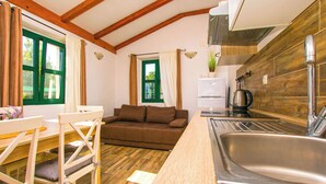 A compact kitchen with a sink, a dining table with chairs, a sofa, and a window with curtains. - Apartments Tarragon (Ugrinic)