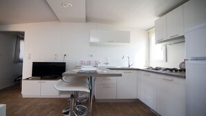 A modern kitchen with white cabinets, a built-in stove, a sink, and a flat-screen TV. - Mobile Home Frangipani 1 (Biograd)